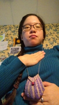 Anti-stress position demo: a photo of a brunette girl wearing a turquoise turtleneck. She has one hand on her chest around the breastbone area, and one hand on her stomach.